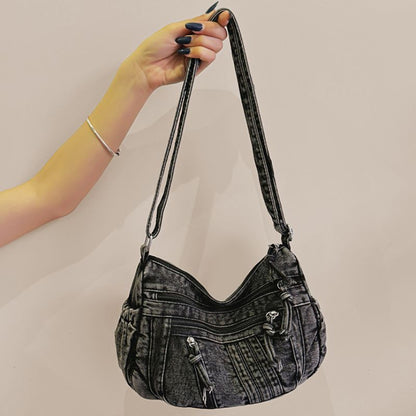 Hand holding a black denim handbag against a plain background