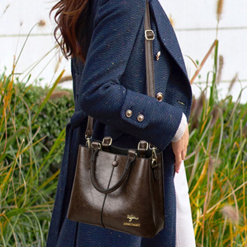 Person wearing a navy coat with a brown leather handbag in an outdoor setting