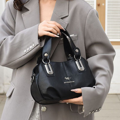 Person holding a black handbag with a visible brand logo, wearing a gray coat.