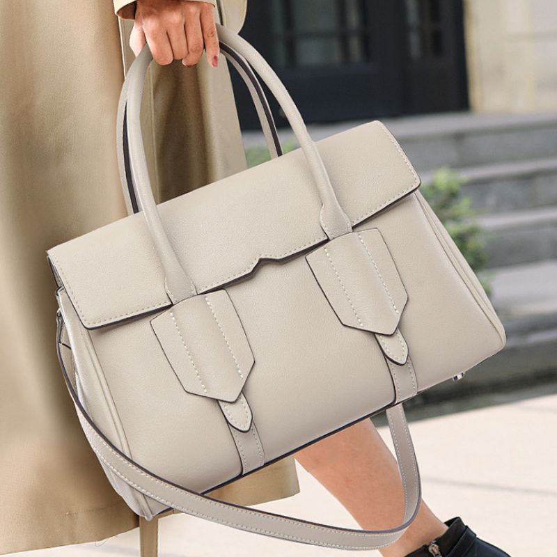 Light gray handbag held by a person wearing a beige coat.