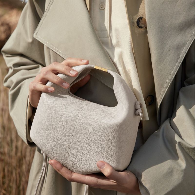 Person holding a textured beige handbag with a blurred natural background
