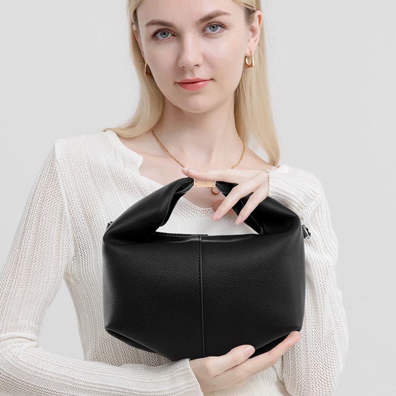 Woman holding a black leather handbag against a plain background