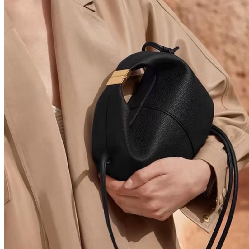 Person holding a black leather bag with a beige coat