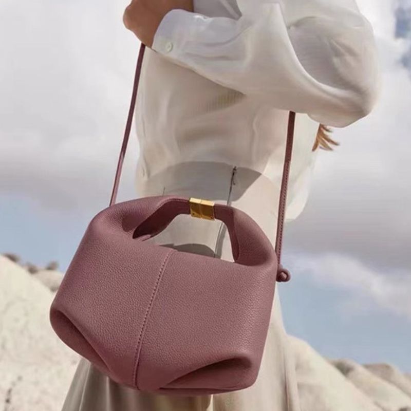 Pink handbag held by a person wearing a white shirt with a blurred natural background