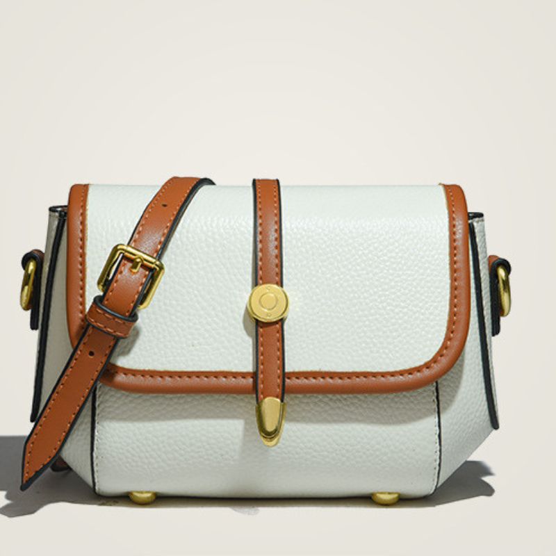 White handbag with brown leather straps and gold buckles on a beige background