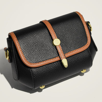 Black leather bag with brown strap and gold hardware on a beige background