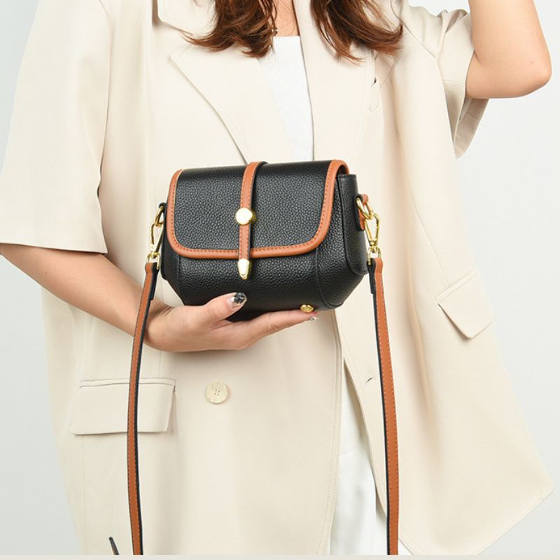 Person holding a black handbag with brown straps against a light background