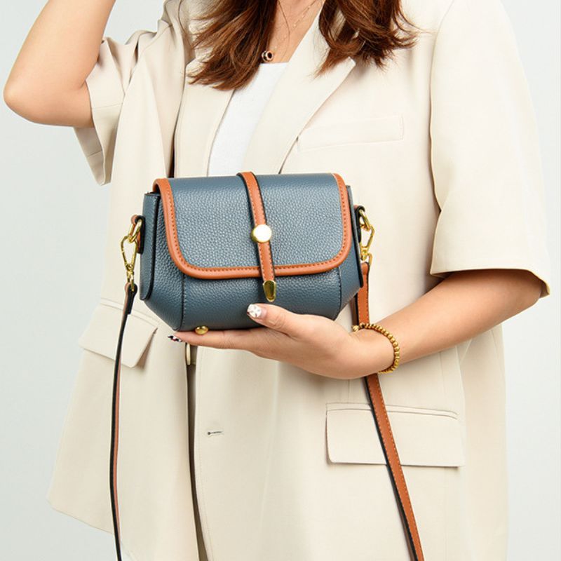 Person holding a blue handbag with brown accents against a light background