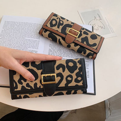Leopard print wallet with gold buckle held by a hand on a table with an open book.