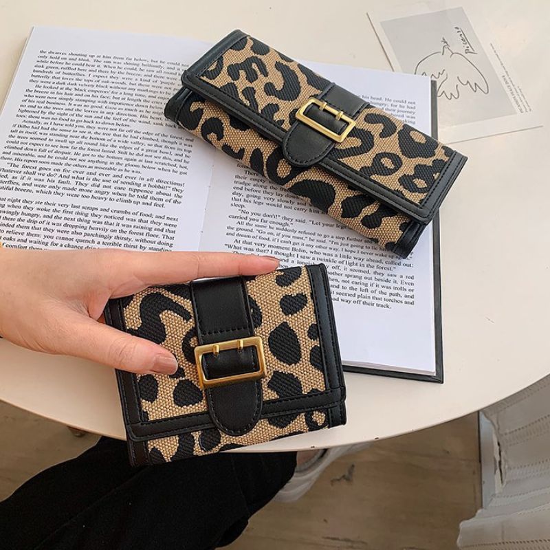 Leopard print wallet with gold buckle held by a hand on a book