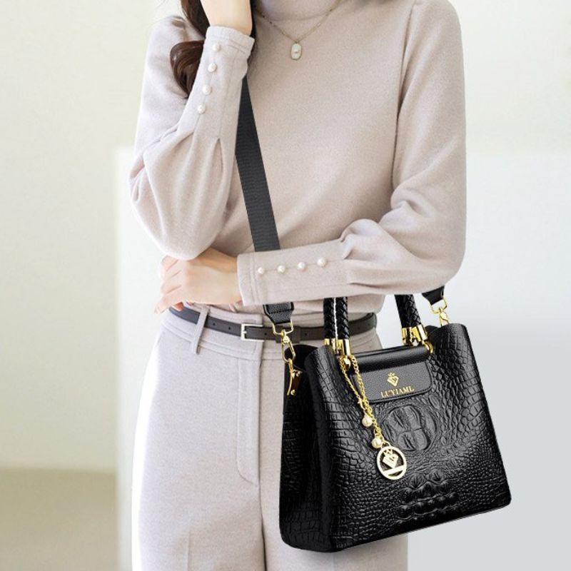Person wearing a beige sweater and light gray pants with a black handbag featuring gold accents.