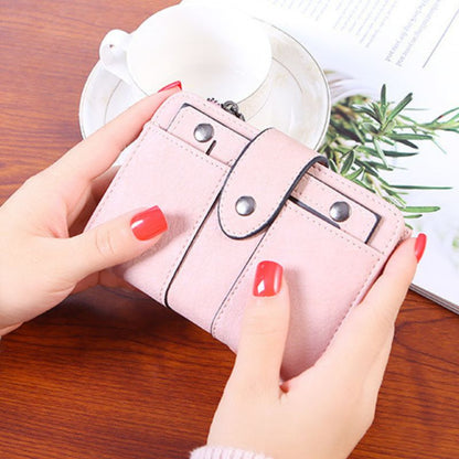 Pink wallet held by hands with red nail polish on a wooden surface.