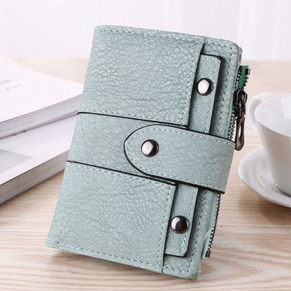 Light blue wallet with button details on a wooden surface with a cup and book in the background
