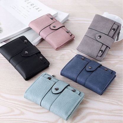 Five different colored wallets (black, pink, gray, blue, and green) on a wooden surface.