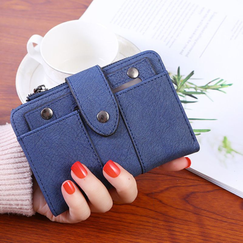 Blue wallet held by a hand with red nail polish on a wooden surface.