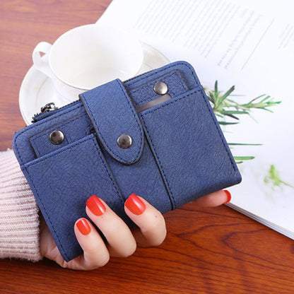 Blue wallet held by a hand with red nail polish on a wooden surface.