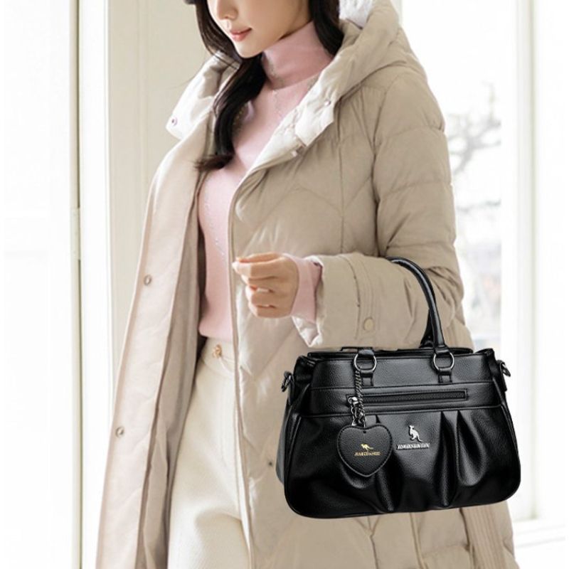 Woman holding a black handbag with a heart-shaped tag, wearing a beige coat.