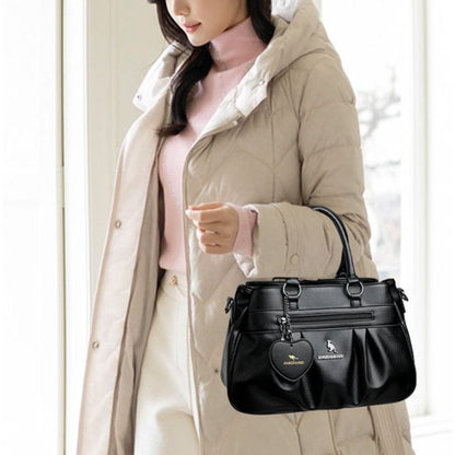 Woman holding a black handbag with a heart-shaped tag, wearing a beige coat.