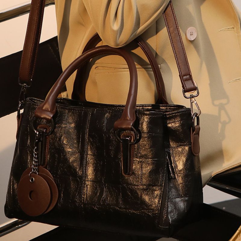 Brown leather handbag with matching strap and decorative elements on a neutral background