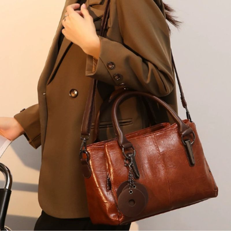 Brown leather handbag held by a person wearing a brown coat.