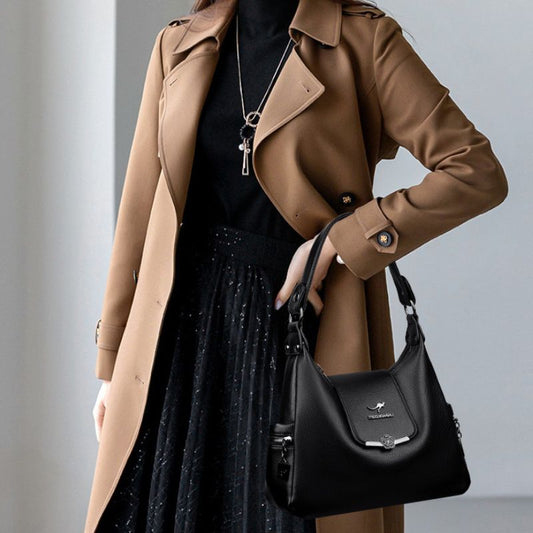 Person wearing a brown coat holding a black handbag against a neutral background