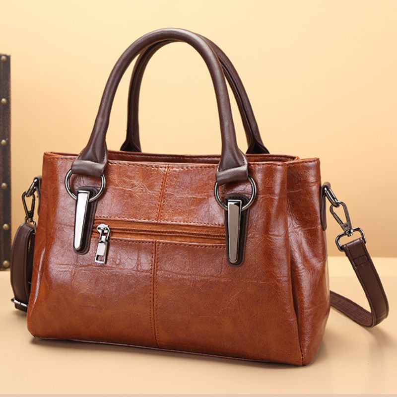 Brown handbag with silver zippers on a beige background