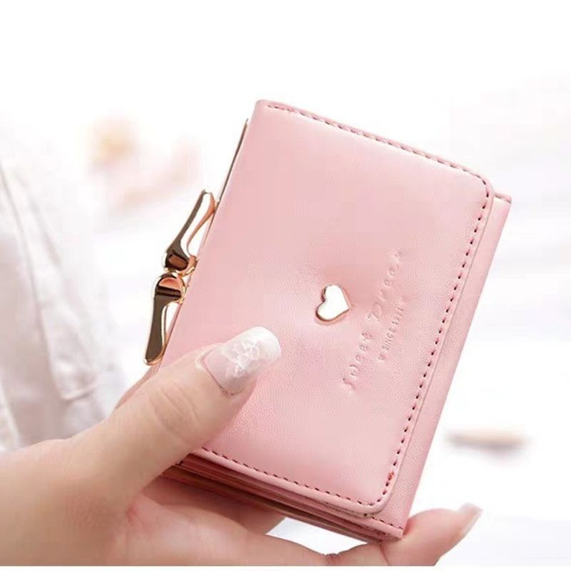 Pink wallet with a heart cutout held by a hand against a blurred background