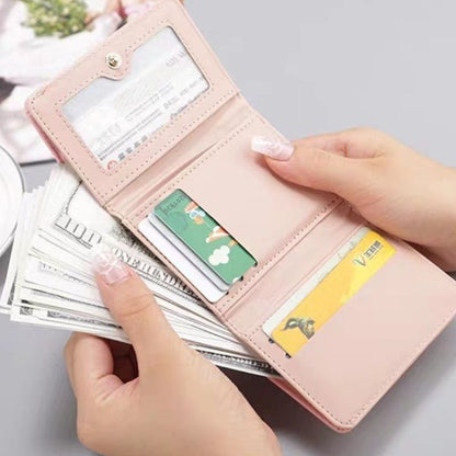 Pink wallet with money and cards held by a hand on a light gray background