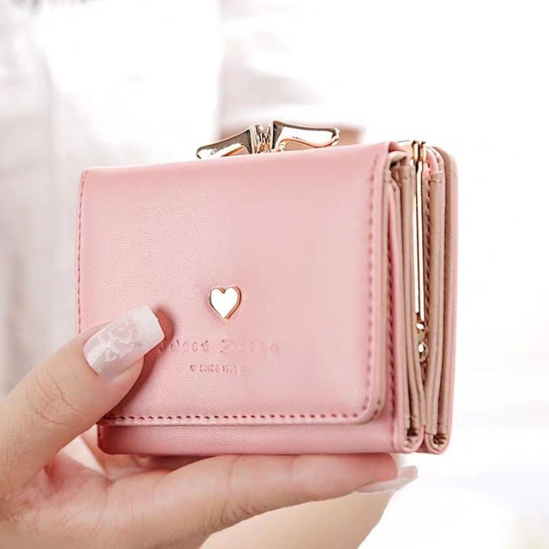 Pink wallet with a heart design held by a hand against a white background