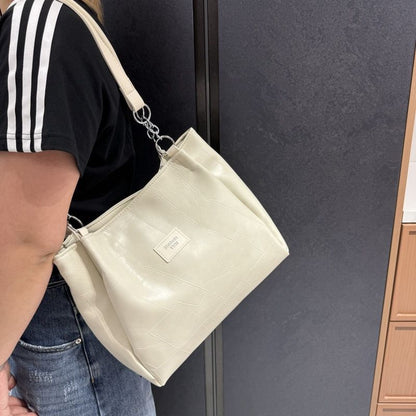 Person holding a beige handbag with a visible brand logo against a dark background