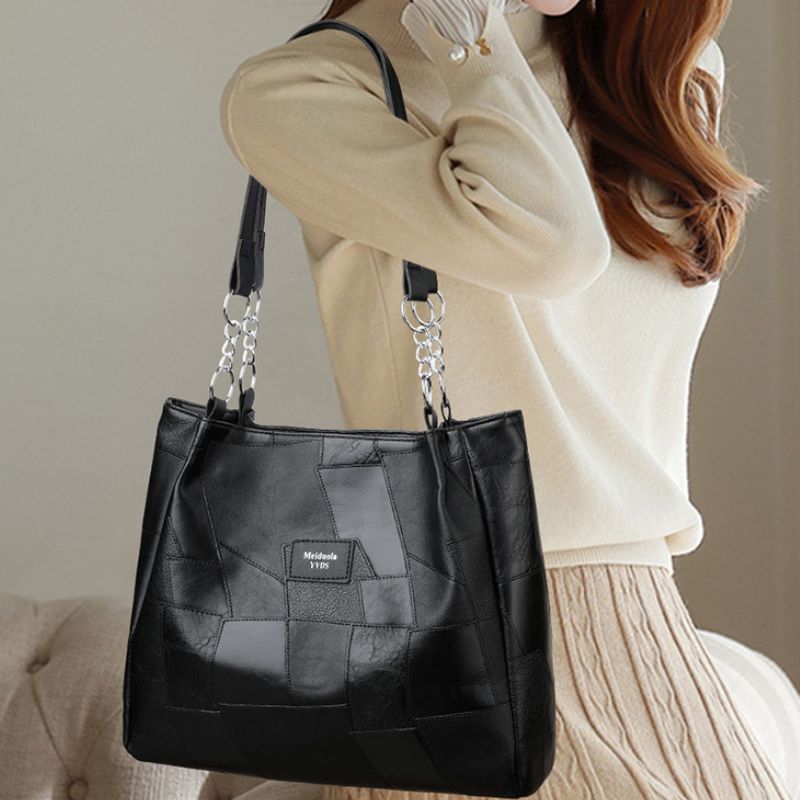 Black quilted handbag with chain detail held by a person wearing a beige sweater.