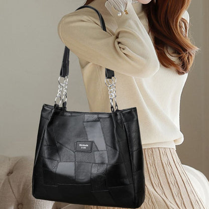 Black quilted handbag with chain detail held by a person wearing a beige sweater.