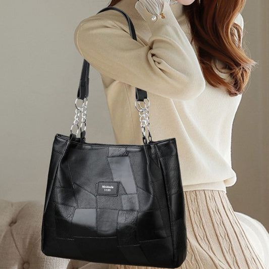Black quilted handbag with chain detail held by a person wearing a beige sweater.