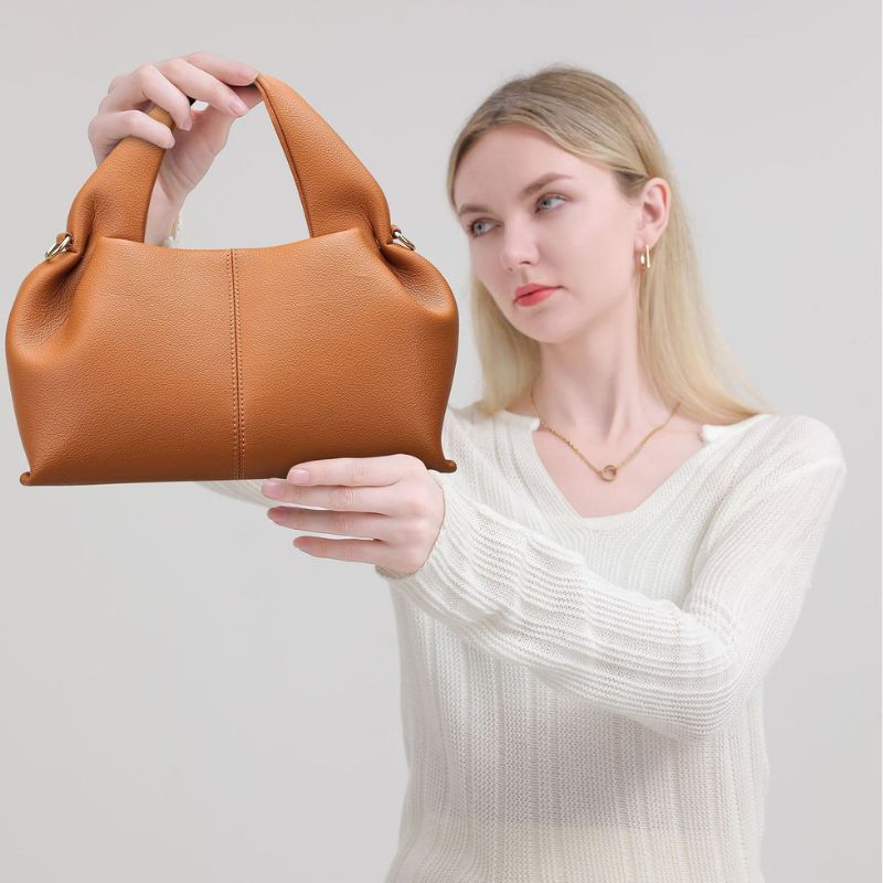 Woman holding a brown leather handbag against a plain background