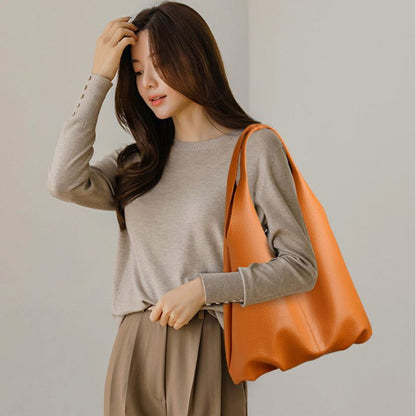 Woman holding an orange bag against a plain background