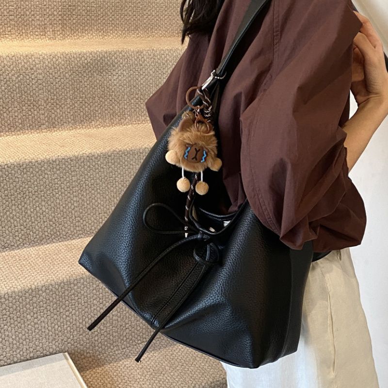 Woman hanging soft leather handbag with plush toy keyring on strap.