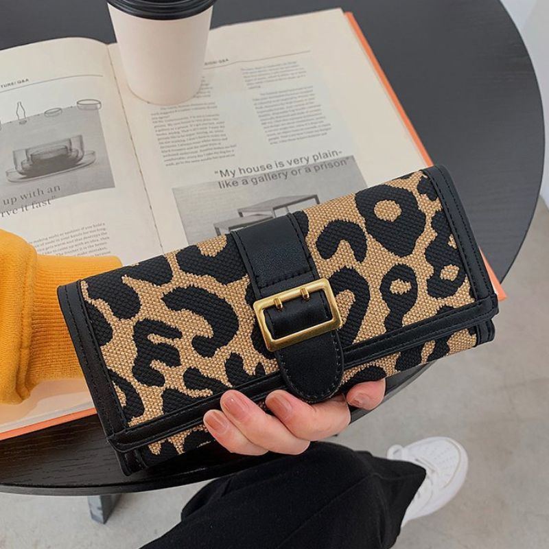 Leopard print wallet held by a person with a book and coffee cup in the background