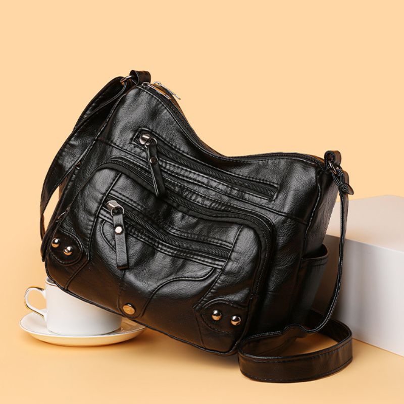 Black leather handbag on a beige background with a cup and saucer.