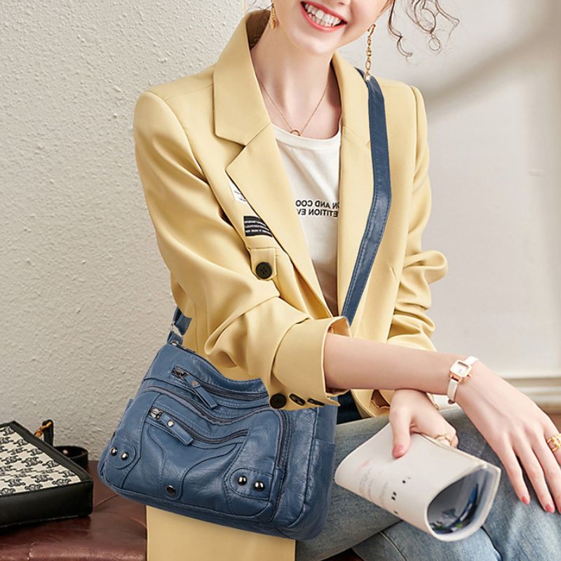 Woman wearing a yellow blazer holding a blue handbag indoors.