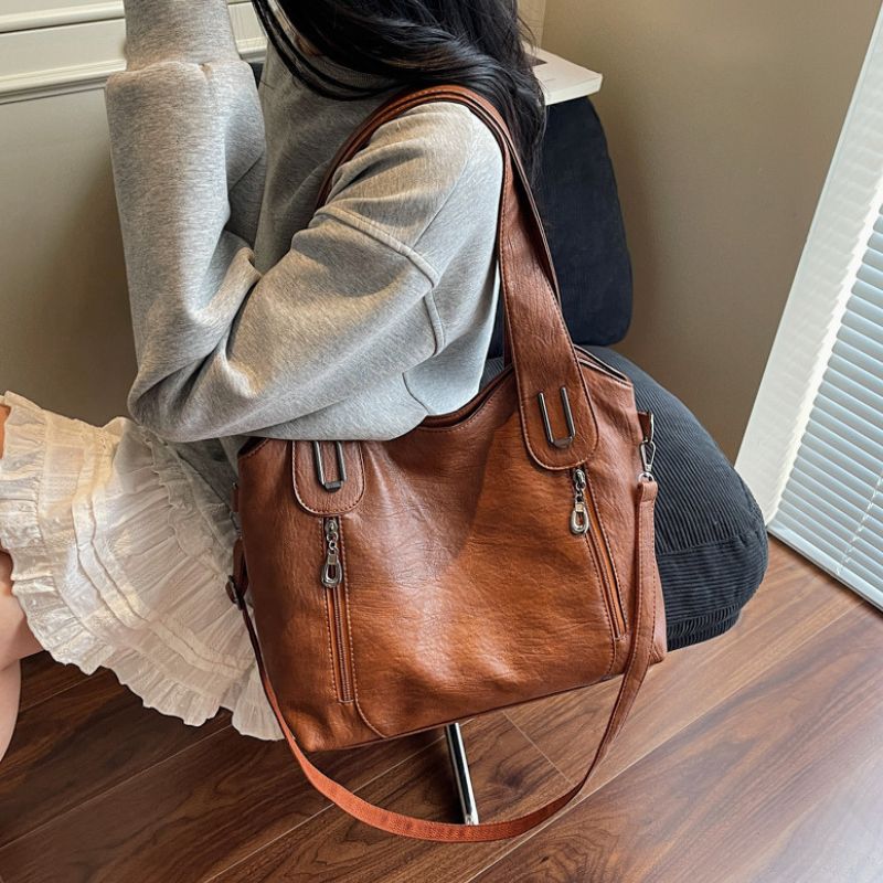 Person holding a brown leather handbag on a wooden floor.