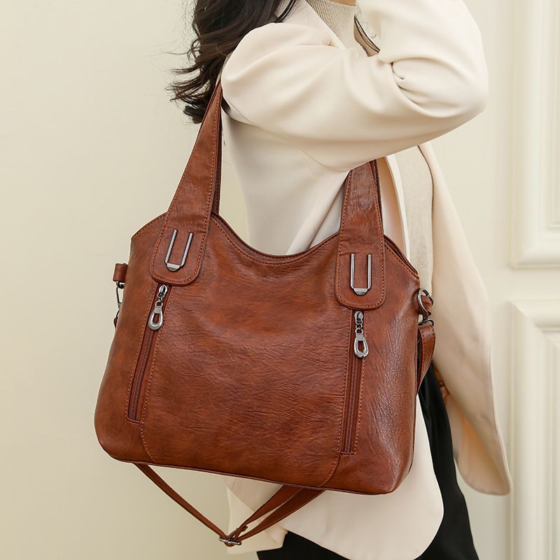 Brown handbag with zippers held by a person wearing a white sweater.
