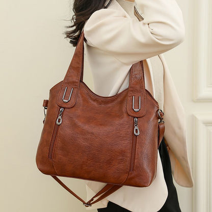 Brown handbag with zippers held by a person wearing a white sweater.