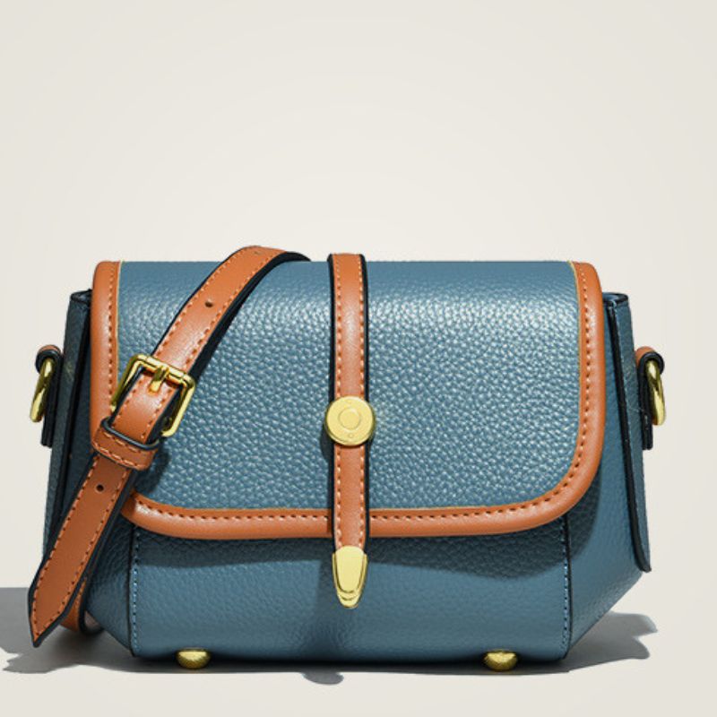 Blue leather bag with brown strap and gold hardware on a beige background