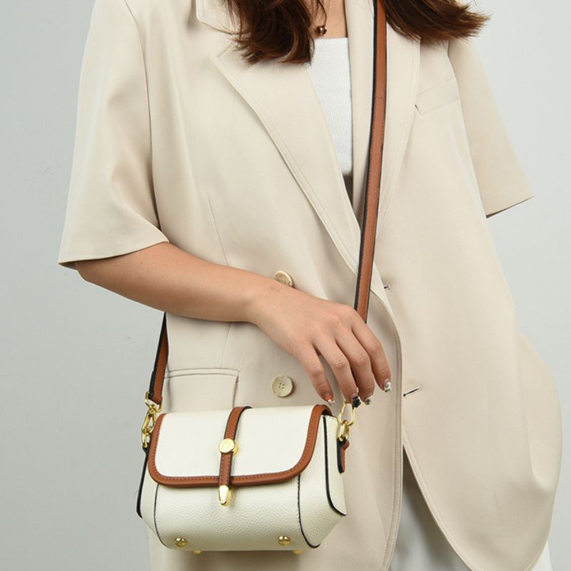 Person wearing a beige blazer holding a white handbag with brown accents.