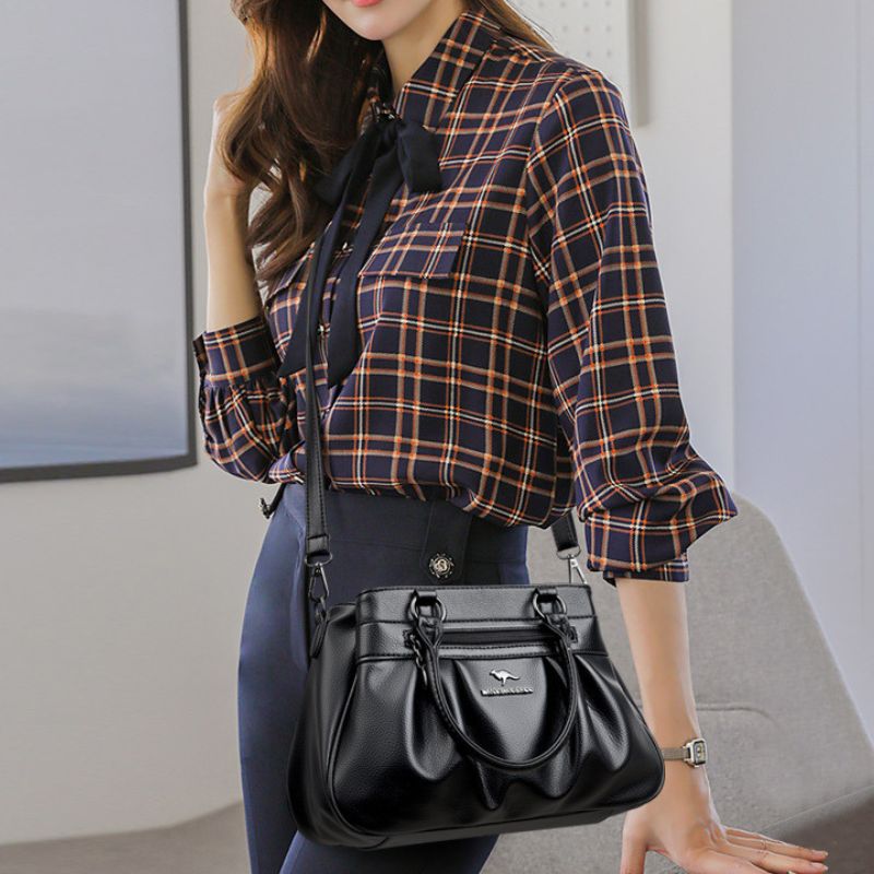 Woman wearing a plaid shirt and holding a black handbag indoors.