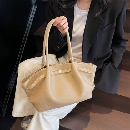 Beige handbag held by a person wearing a black coat and white pants.