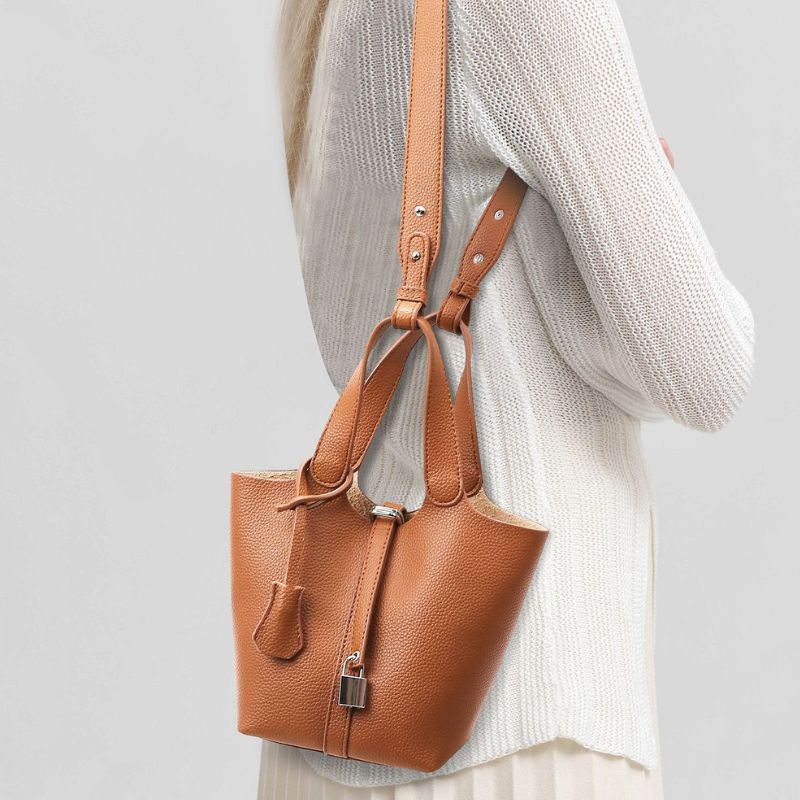 Brown leather handbag held by a person wearing a light gray sweater on a plain background