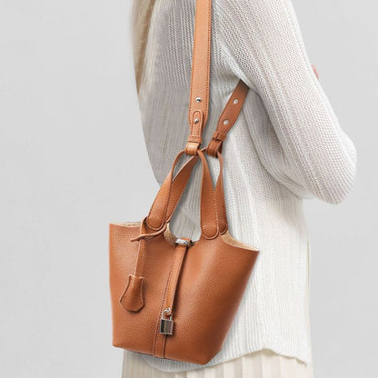 Brown leather handbag held by a person wearing a light gray sweater on a plain background