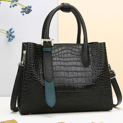 Black crocodile-patterned handbag with a blue strap on a light background
