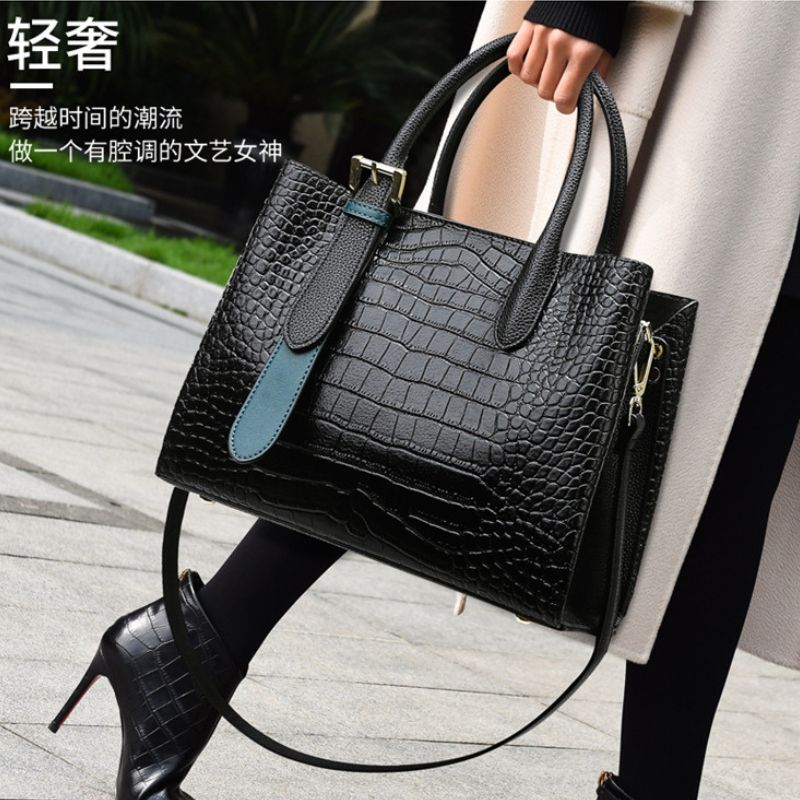 Black textured handbag with blue accents held by a person on a sidewalk.